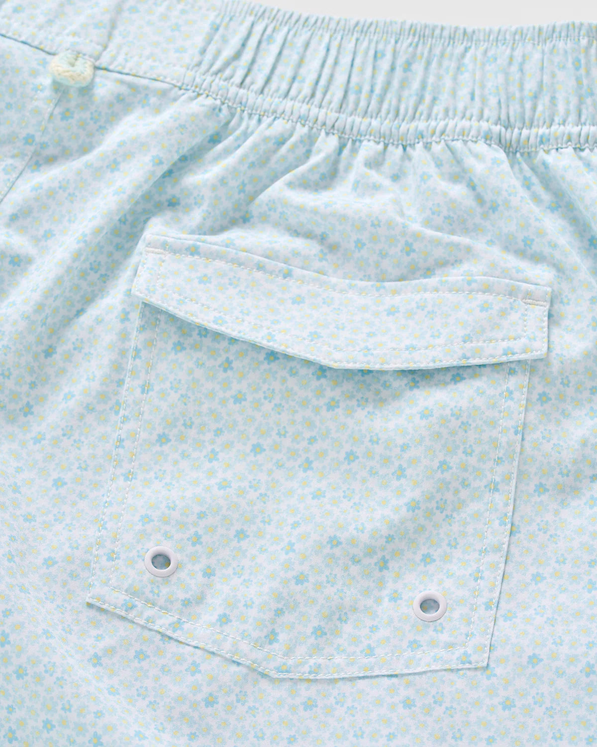 Close-up of the Anemone Swim Trunks by Johnnie-O, made from a light blue patterned poly/spandex blend. These comfortable surf shorts feature an elastic waistband and a back pocket with two metal grommets—perfect for easy-wearing style and fun, vibrant prints.