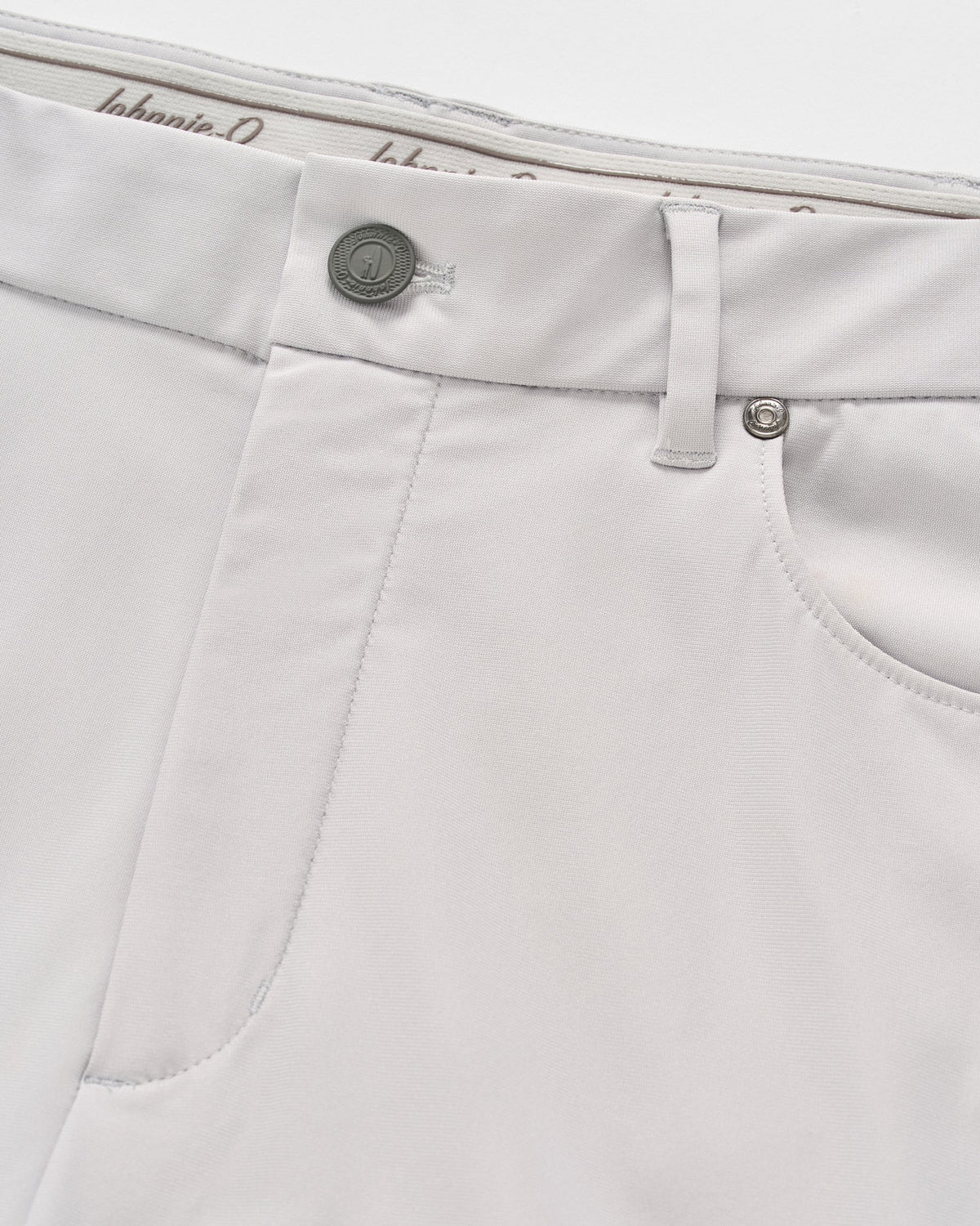 Close-up of the front pocket and waistband on a pair of light gray Johnnie-O Cross Country Flex Pants, crafted from stretch knit fabric with a button, belt loop, and visible stitching details.