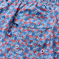 Close-up of the pocket on the Johnnie-O Freesia Swim Trunk, featuring blue fabric with a lively red, white, and blue floral print—ideal for anyone who loves fun patterns. The pocket includes metal eyelets and a buttoned flap, adding classic surf short-inspired functionality.