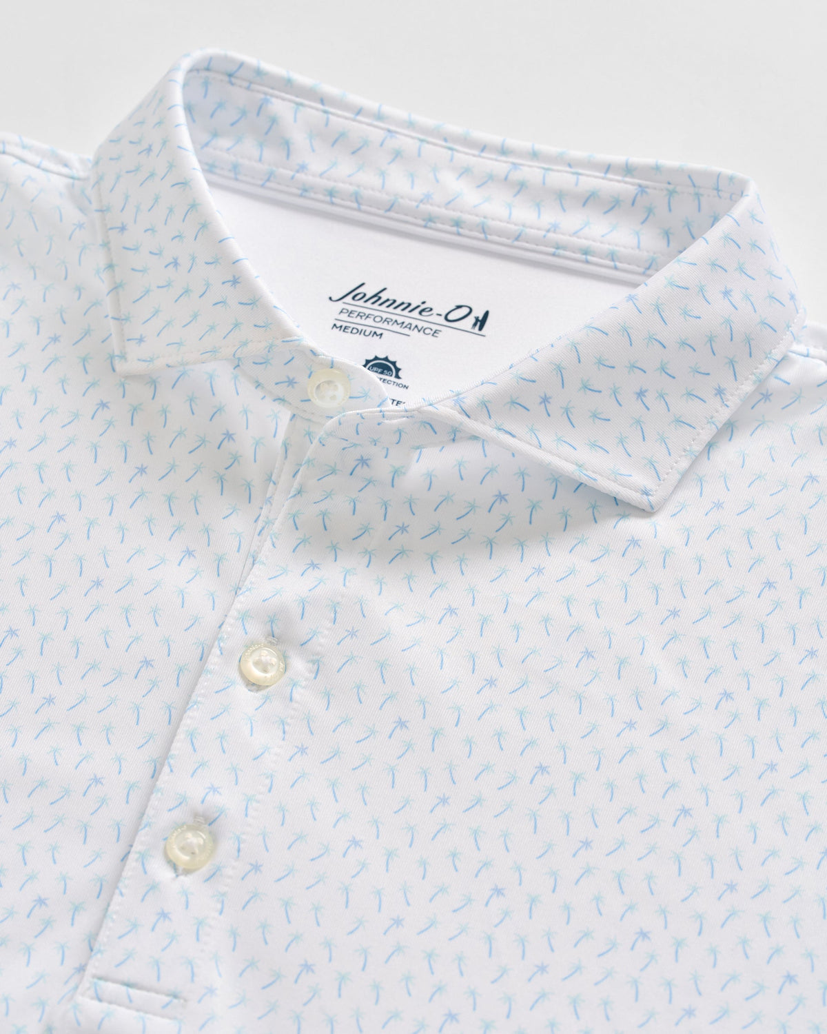 Close-up of a white Johnnie-O Marina Polo with a light blue small pattern and buttons, made from moisture-wicking fabric and featuring the brand label inside the collar.