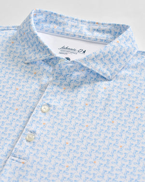 Johnnie-O Minty Polo: A light blue short-sleeve men's performance polo shirt featuring a subtle pattern of blue and orange illustrated sea creatures, partial button placket, and a visible Johnnie-O brand label inside the collar.