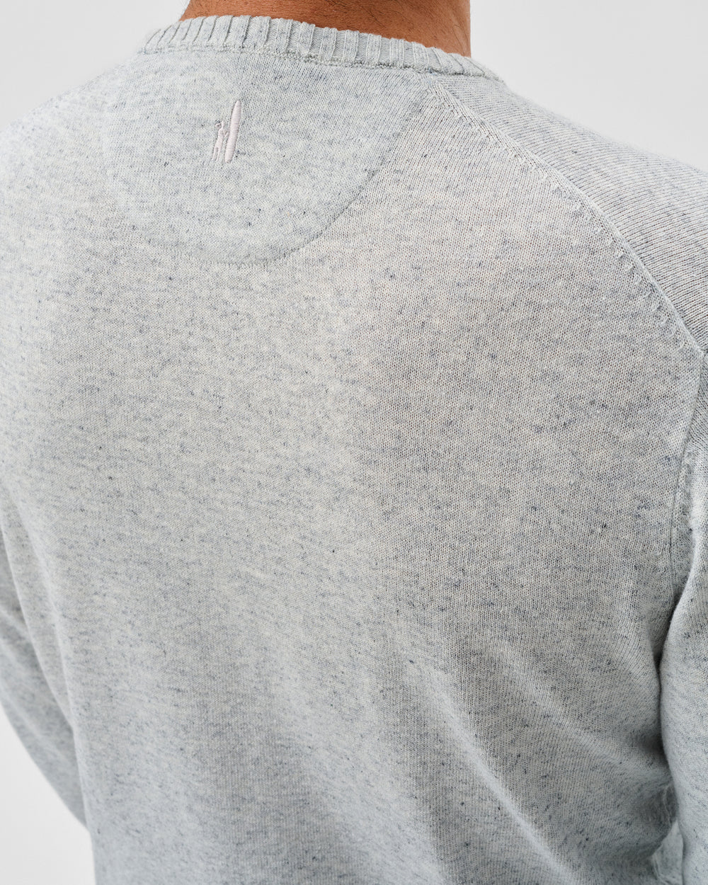 Close-up of a person's back wearing the Johnnie-O Albus Crew, a light gray, speckled knit ultrasoft crewneck sweater featuring a visible seam detail near the neckline—perfect for everyday layering.