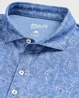Close-up of the Johnnie-O Osmond Polo, a blue collared shirt adorned with a white tropical leaf and flamingo pattern. Crafted from lightweight, moisture-wicking fabric for all-day comfort, this polo features button details and a “johnnie-O Performance Medium” tag. With UPF 50 protection, the Osmond Polo is an ideal choice for sunny days.