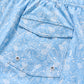 Close-up of Johnnie-O Swingin Swim Trunks, featuring a vibrant blue and white tropical pattern, an elastic waistband, and a flap pocket with metal eyelets—ideal for fans of playful prints.