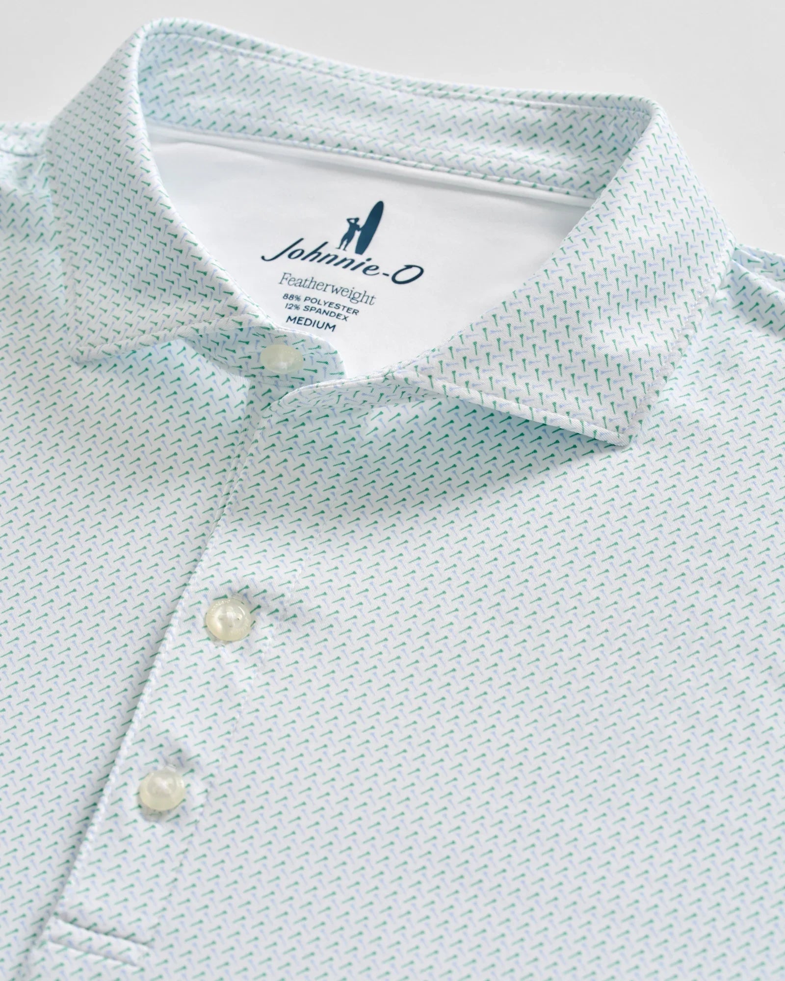 Close-up of a light blue Johnnie-O Tee Party Polo featuring a subtle geometric pattern, three white buttons, and a visible collar and tag indicating size medium. This polo offers moisture-wicking fabric and UPF 50 sun protection for all-day comfort and coverage.