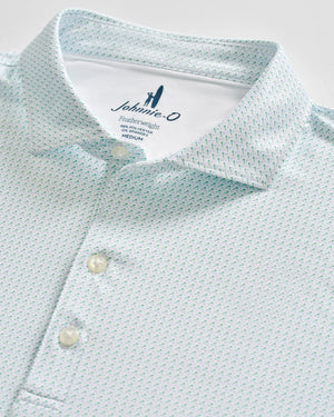 Close-up of a light blue Johnnie-O Tee Party Polo featuring a subtle geometric pattern, three white buttons, and a visible collar and tag indicating size medium. This polo offers moisture-wicking fabric and UPF 50 sun protection for all-day comfort and coverage.
