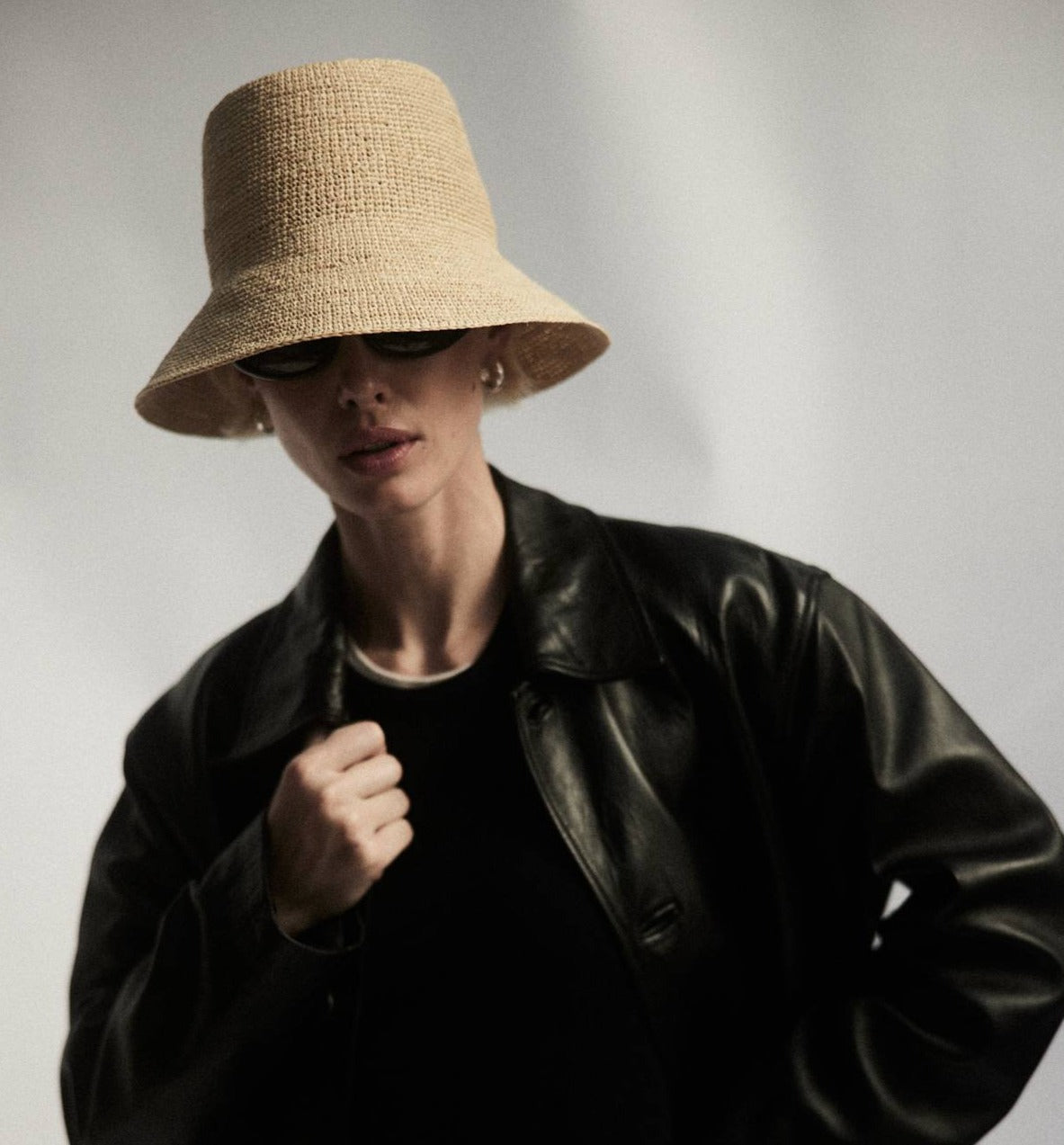 A person in a black leather jacket and a wide-brimmed Janessa Leone Felix Hat, wearing sunglasses, poses against a light background.