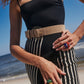 A person wearing a black top, a striped skirt with a Lizzie Fortunato Louise Belt, and colorful rings standing on a beach.