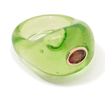 The Monument Ring by Lizzie Fortunato is a translucent green resin cocktail ring with a rounded shape, accented by an oval gemstone in a gold bezel—an eye-catching statement piece.