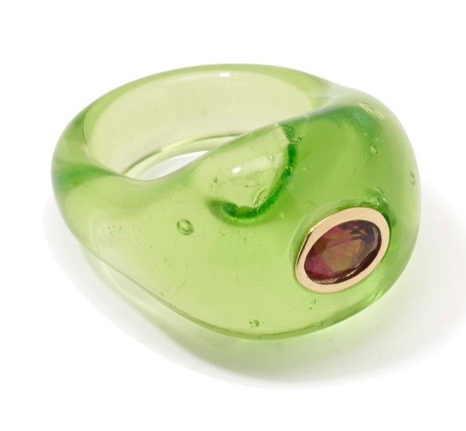 The Monument Ring by Lizzie Fortunato is a translucent green resin cocktail ring with a rounded shape, accented by an oval gemstone in a gold bezel—an eye-catching statement piece.