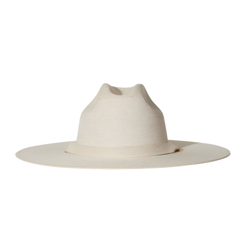 The Palmer Hat by Janessa Leone is a wide-brimmed, light beige palm straw hat featuring a pinched crown and organic cotton ties with regenerative leather aglets, photographed on a plain white background.