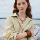 A woman with long red hair stands outdoors near water and rocks, wearing a beige shirt and the Lizzie Fortunato Ridge Cuff—chunky gold and brown jewelry.