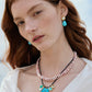 A woman with fair skin and long red hair wears a white blouse, turquoise bead drops, and Lizzie Fortunato's Rock Pool Earrings, paired with layered necklaces featuring pink beads and a turquoise flower pendant.