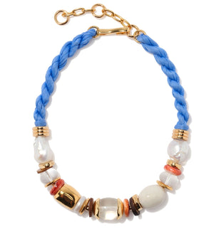 The Glass Beach Necklace by Lizzie Fortunato features a braided blue cord, gold-plated chain, and assorted gold, pearl, white, and coral-colored beads.