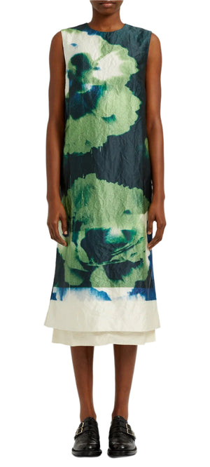 The individual is sporting an Erdem Sleeveless Pencil Midi Dress with a striking green and blue carnation-inspired floral pattern on a white base, paired with black shoes.