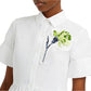 The person is wearing Erdem's Short Sleeve Embroidered Shirt Dress—a white collared shirt dress with green and white embroidered carnations on the chest, adding elegance.