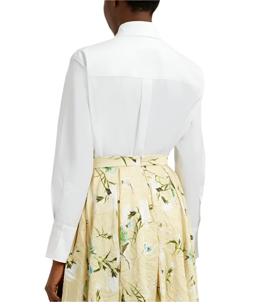 An individual is seen from behind wearing an oversized white Long Sleeve Embroidered Shirt by Erdem, tucked into a high-waisted, yellow floral skirt.