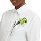 A person is wearing an oversized white Long Sleeve Embroidered Shirt by Erdem, featuring a detailed green and blue flower embroidery on the left chest.