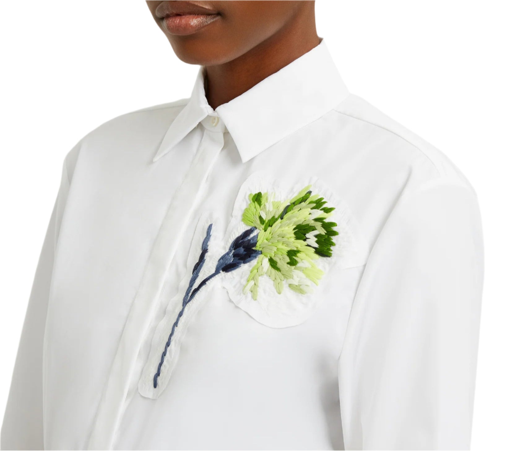 A person is wearing an oversized white Long Sleeve Embroidered Shirt by Erdem, featuring a detailed green and blue flower embroidery on the left chest.