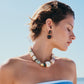 A woman with short hair stands outdoors against a clear blue sky, wearing a striped strapless top and Lizzie Fortunato's Nopales Earrings.