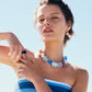 A woman wearing the Lizzie Fortunato Delphine Collar, a striped blue and white top, and gold hoop earrings poses outdoors against a clear blue sky.