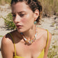 A woman outdoors wears a yellow sleeveless top, square earrings, and the Lizzie Fortunato Glass Beach Necklace, featuring colorful beads and freshwater pearls, with grass and sand in the background.