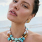 A woman wearing gold earrings and the Lizzie Fortunato Ariel Necklace—featuring double strands of turquoise, freshwater pearl, and gold beads—poses outdoors by the beach.