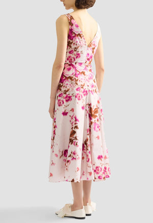 A woman faces away wearing the Erdem Rose Bouquet Fit and Flared Midi Dress, a sleeveless cotton poplin midi dress with pink rose prints and a V-back, paired with white shoes.