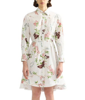 A woman wears the Erdem French Chintz Mini Shirt Dress, a long-sleeved white cotton poplin design with a pink, green, and purple floral print, finished with a collar and front button closure.