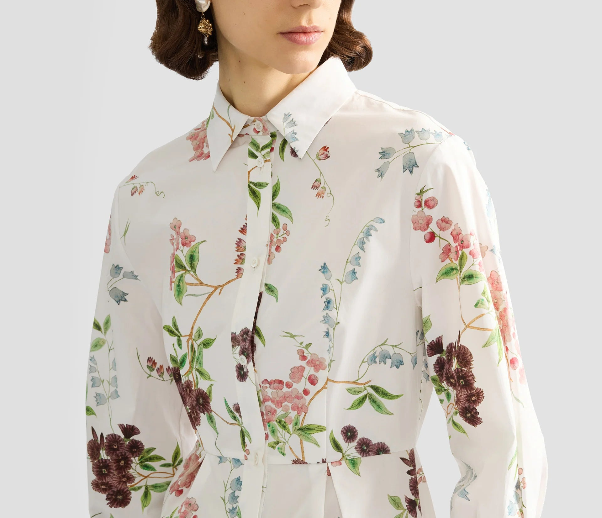 A woman wears the Erdem French Chintz Mini Shirt Dress, a collared, long-sleeve cotton poplin dress with a colorful floral print, shown from shoulders to waist.