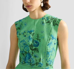 A woman accessorized with pearl drop earrings adds fresh charm to the Erdem Rose Bouquet Linen Pencil Midi Dress, a sleeveless green midi featuring blue floral print and decorative vertical seams.