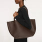 Dressed in black, a person carries the spacious Everyday Soft Tote by Mansur Gavriel over their shoulder against a plain background.