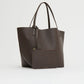The Mansur Gavriel Everyday Soft Tote in dark brown leather, featuring thin handles, is displayed on a plain light background with a matching zippered pouch placed in front.