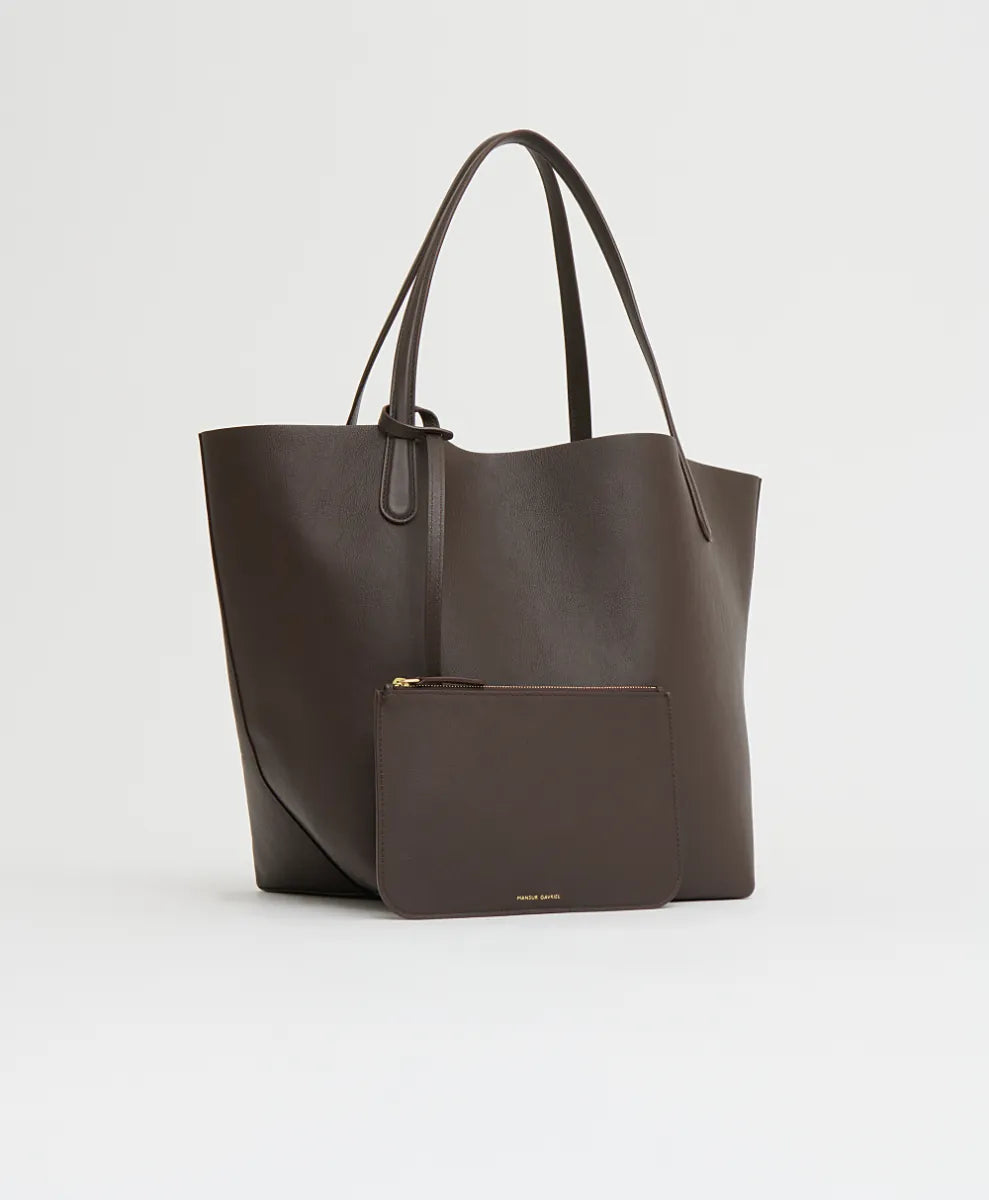 The Mansur Gavriel Everyday Soft Tote in dark brown leather, featuring thin handles, is displayed on a plain light background with a matching zippered pouch placed in front.