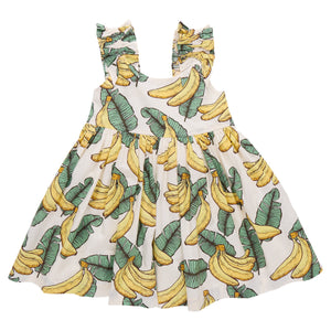 The Girls' Via Dress by Pink Chicken is a white sleeveless cotton cambric dress with ruffled, adjustable straps and a playful tropical banana and green leaf print.