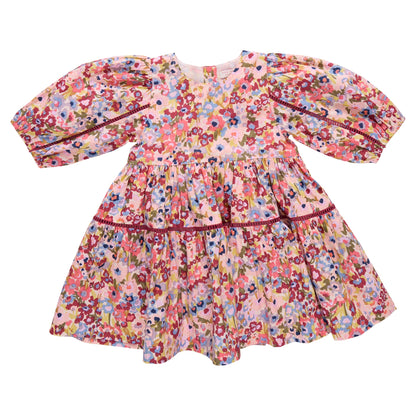 The Girls' Maribelle Dress by Pink Chicken features puffy long sleeves, a flared skirt, and a colorful floral print in pink, red, blue, and yellow—perfect as a spring dress for your little one.