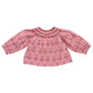 The Girls' Ava Top by Pink Chicken features a pink strawflower block print, smocked neckline, and loose gathered long sleeves. Shown on a white background.