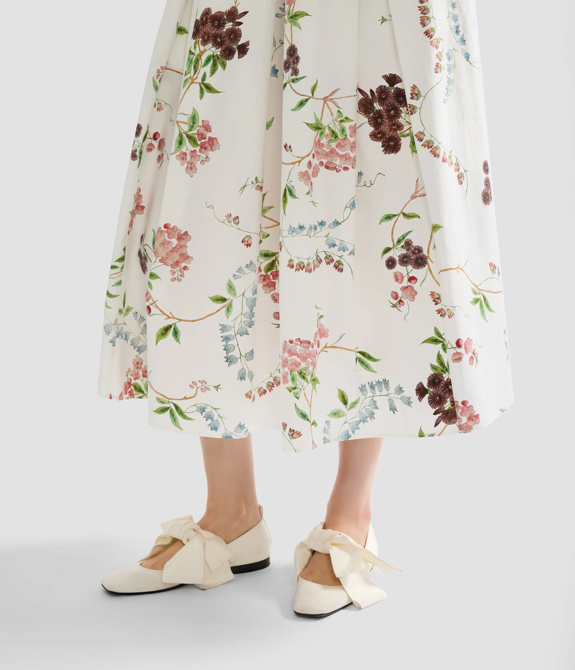 A person wearing the Erdem French Chintz Cotton Midi Skirt and cream flats with large bows stands on a light surface.