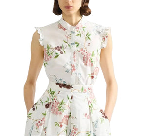 A woman wears the Erdem French Chintz Cotton Sleeveless Shirt, featuring a white floral print, buttoned front, and ruffled shoulders—ideal to pair with a chic white cotton or floral blouse.