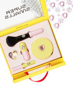 The Super Smalls Mom's Makeup Play Kit is a yellow kids set with brushes, lip products, a compact, nail accessories, and rhinestones. A sheet of rhinestone stickers appears in the background. Safe makeup designed for children to enjoy.