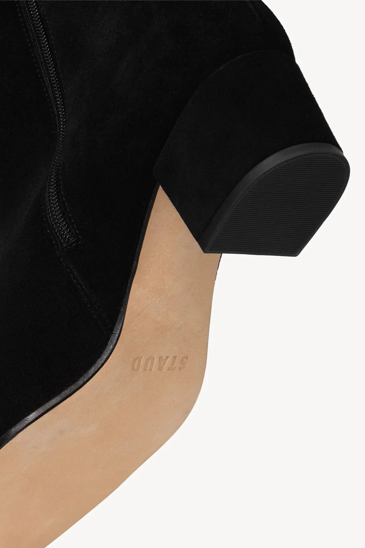 Close-up of the Staud Aimee Short Boot, a black suede ankle bootie with a side zipper, featuring a tan sole and the brand logo stamped on the bottom.