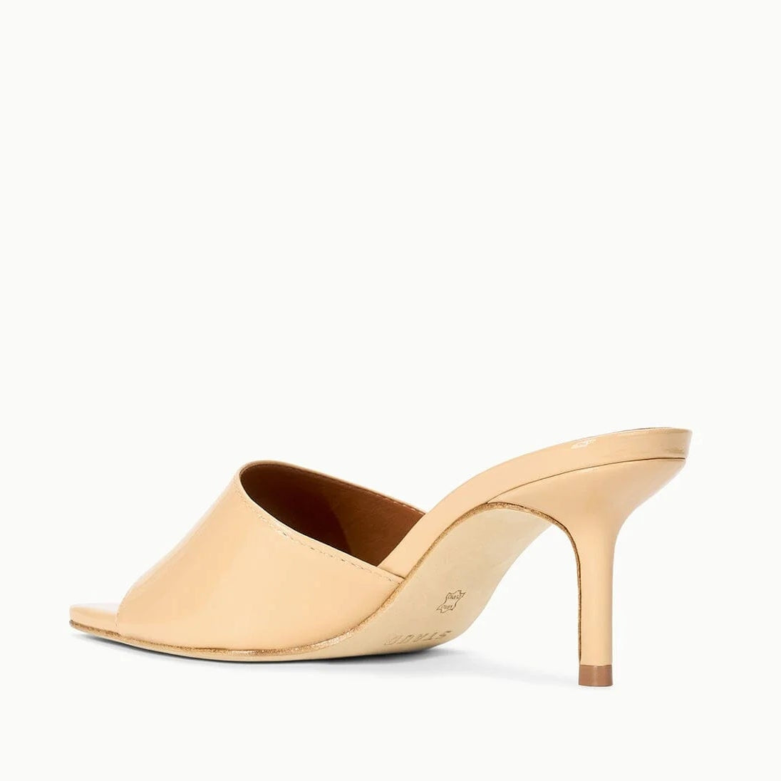 The Staud Bea Mule is a high-heeled leather mule featuring a square toe and glossy finish, seen from the back against a white background.