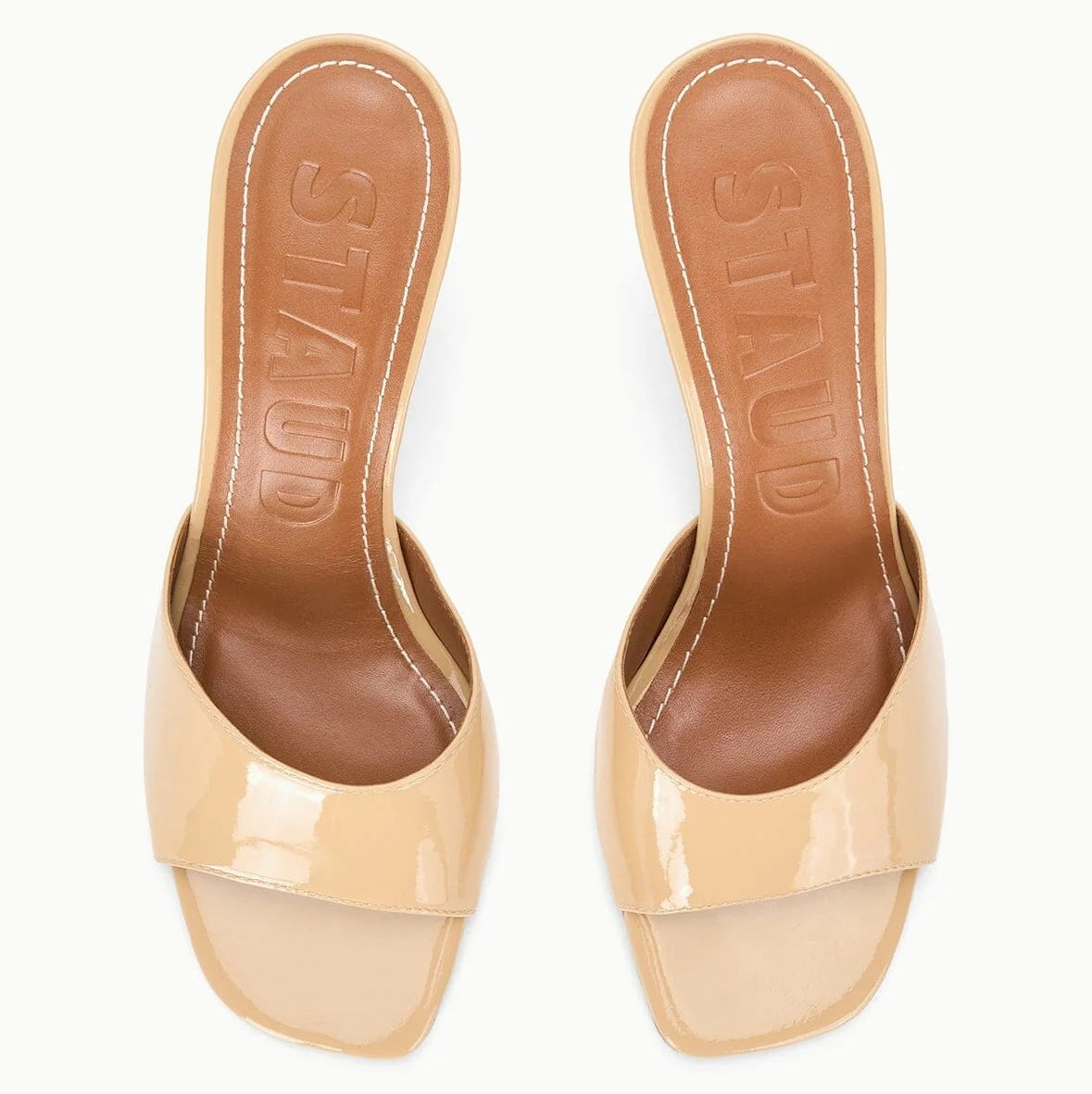 A pair of beige, open-toe Bea Mule heeled sandals by Staud, featuring a square toe and "STAUD" embossed on the brown insoles.