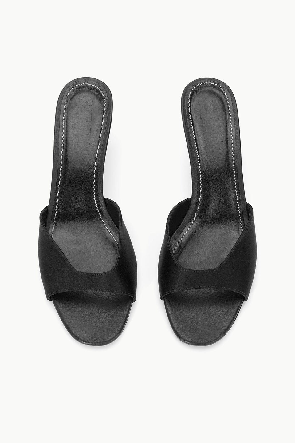 The Staud Brigitte Satin Mule is a black open-toe heeled mule with a wide front strap and stitched insole, perfect for versatile dressing, shown against a white background.