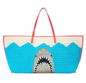 The Christos Large Tote by Staud features a spacious woven design with red handles and a bold shark motif, displaying an open mouth and teeth amid blue and white waves.