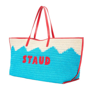 The Christos Large Tote by Staud is a spacious crochet bag featuring red handles, a cream and blue zigzag design, and "STAUD" in red on the front.