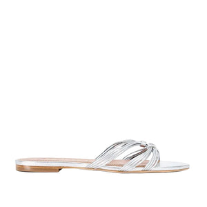 The Staud Carrie Sandal features refined metallic silver leather straps that cross elegantly over the top and a low heel, displayed on a white background.