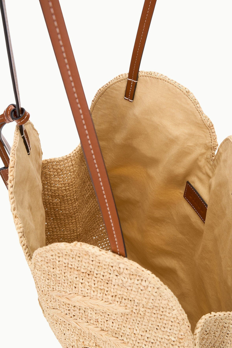 The Staud Large Palm Raffia Bag features open woven straw construction with brown leather shoulder straps and a light tan fabric lining, shown from above to highlight the spacious interior of this elegant carryall.