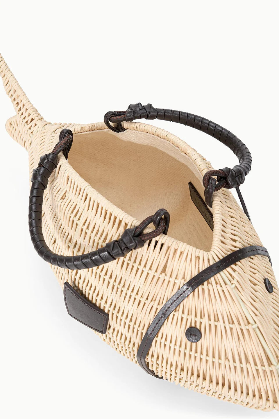 The Cleo Fish Bag by Staud is a woven wicker bag in a fish shape with leather-wrapped handle and detailing, shown from above on a plain background.