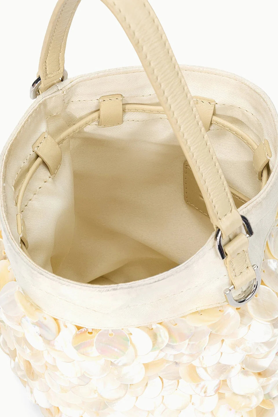 The Lila Mini Bag by Staud is a cream-hued evening bag featuring sequin accents, dual handles, metal hardware, and an open view of its empty beige interior with visible stitching.
